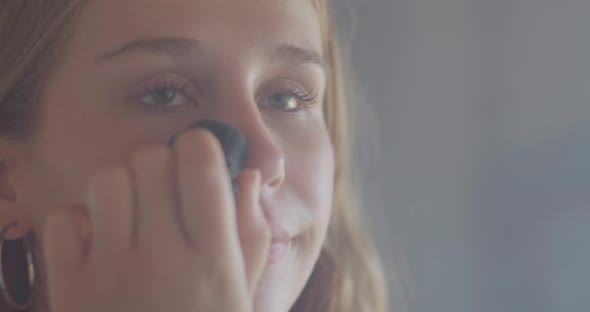 Reflection in the Mirror of a Beautiful Young Woman Putting On Makeup