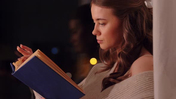 Young Woman Reading Book Sitting at Window