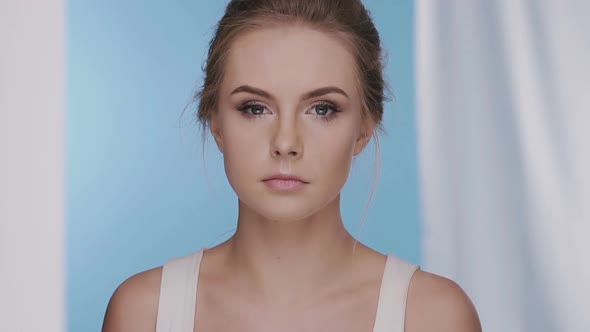 Beautiful Girl Blinking on Blue Background with White Curtains