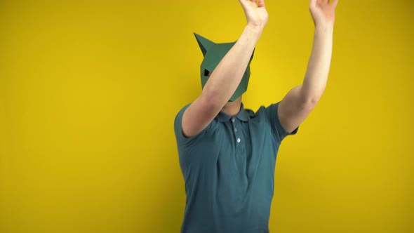 Young Man in a Cardboard Jackal Mask Dances on a Yellow Background. Man in a Green Polo and Mask.