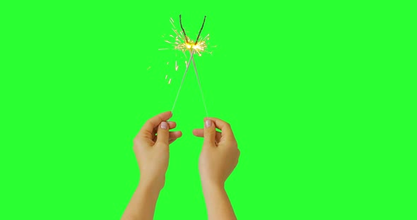 Girl hands holding two fireworks sparklers crossed into X sign on keyed green screen. Holiday.