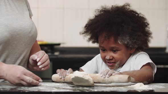 Black Little Girl with Her Mother Rolling Out the Dough in the Kitchen