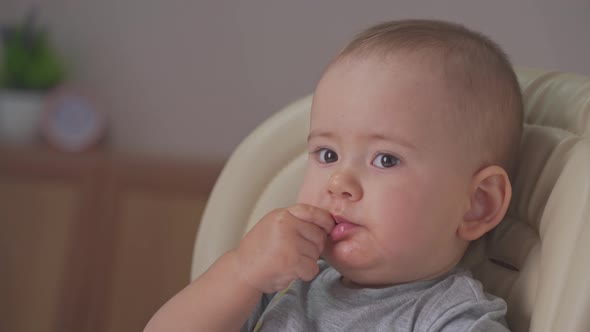 Toddler independently eats spaghetti with his hands while sitting on a feeding chair. close-up