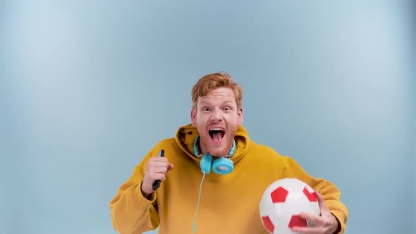 Photo of Funny Lucky Young Man Wear Purple Hoodie Smiling Holding Ball Tv Remote Watching Football