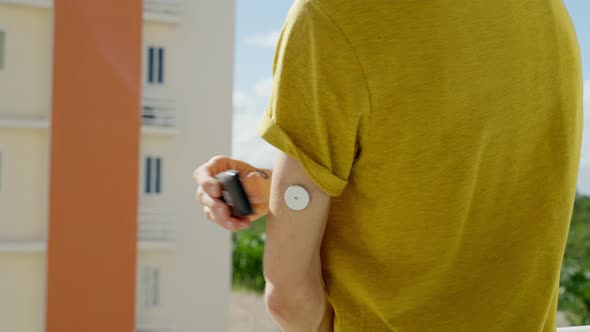 Male Checking His Blood Glucose Levels On Left Arm With Freestyle Libre 2 Sensor On Hotel Balcony
