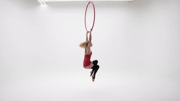 A Girl In A Red Dress Rotates On One Leg Hanging On An Aerial Hoop.