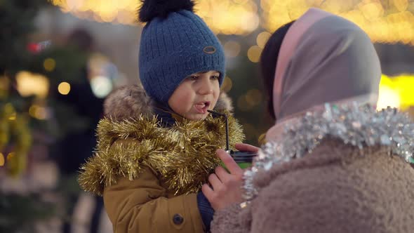 Cute Excited Son Talking with Mother on City Square Decorated for Christmas