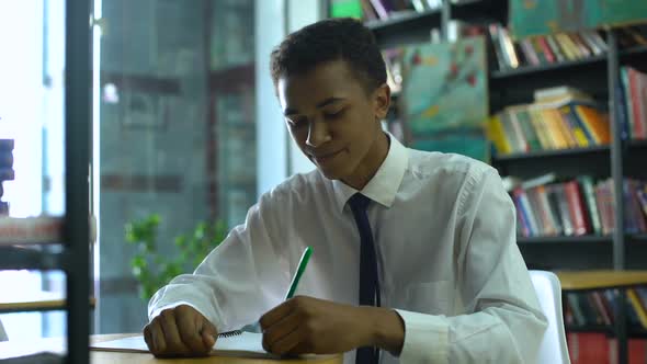 Black Male High-Schooler Thinking About Task, Doing Homework at Campus Library