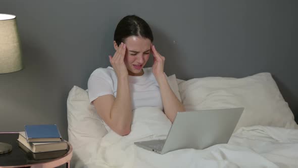 Young Woman with Laptop Having Headache in Bed