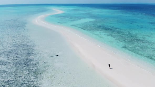 Aerial view of a young man walking at the beach long shoreline in a beautiful small beach island