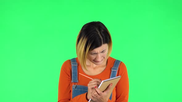 Girl Stands and Thinks, Then Intently Writes with Pencil in Notebook. Green Screen