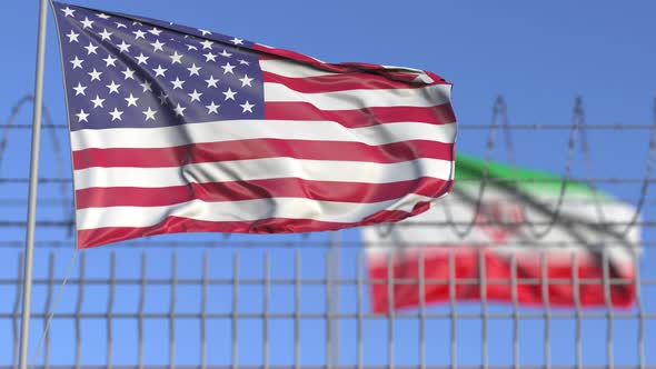 Waving Flags of the USA and Iran Separated By Barbed Wire Fence