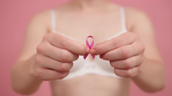 Close Up, Woman Holding Silk Pink Ribbon Between Her Fingers. Breast Cancer Awareness Month Pink