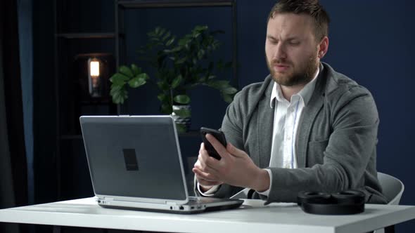 Serious Businessman Using Laptop Computer and Modern Smart Phone for Office Work