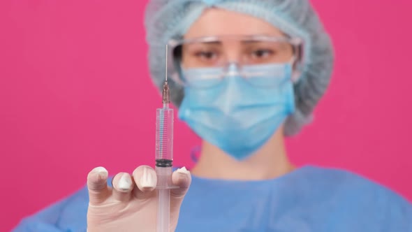 Professional Female Doctor Holds a Syringe with a Vaccine on a Pink Background