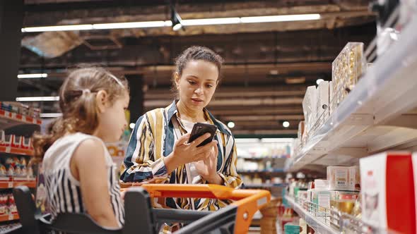 Little Girl Sitting in a Trolley in a Supermarket Asks Her Mother to Buy a Sweet Treat