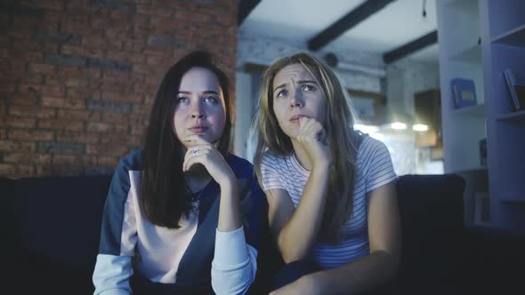 Two Girls Watching Scary Movie or Bad and Unpleasant News at Home. Girlfriends Watch TV Together in