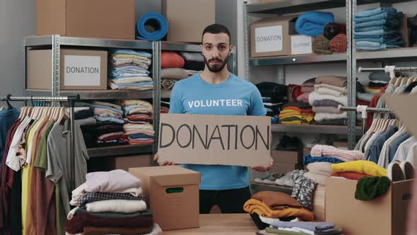 Portrait View of the Caucasian Volunteer Man Holding Cupboard Banner with Donation Word and Looking