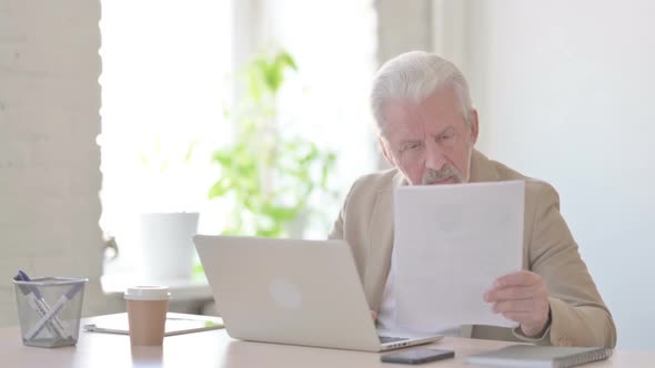 Paperwork By Old Man Working on Laptop in Office