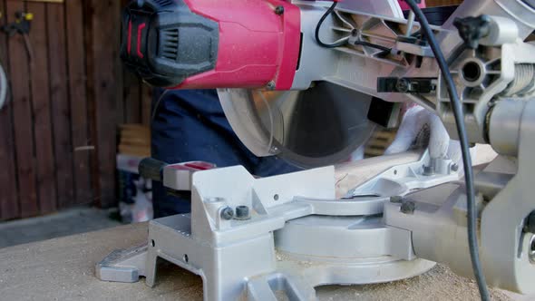 Male Carpenter in Gloves Cuts Off Wooden Workpiece on Mitre Saw Close-up