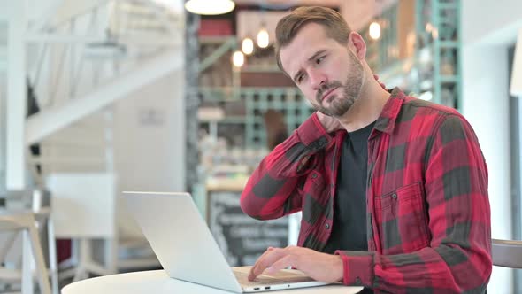 Tired Young Man with Neck Pain Using Laptop in Cafe