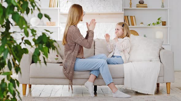 Caucasian Mom Young Adult Woman Playing with Daughter in Patty Cake at Home Sitting on Sofa Mother