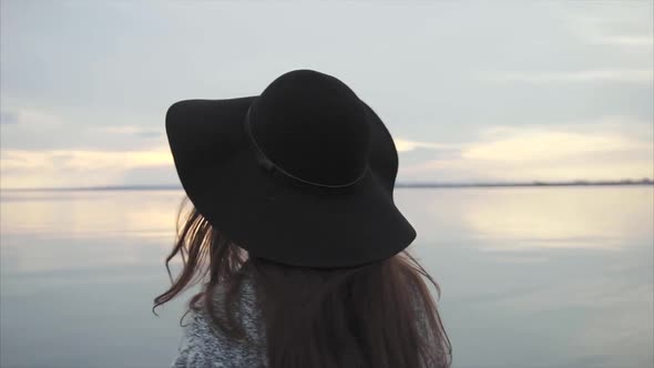 Young Woman in Black Hat and Glasses Near the Sea at Sunset