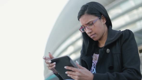 Thoughtful Young Woman Sitting Outdoor with Tablet