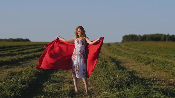 Redhead Woman in White Dress with Red Cloth in Her Hands on Background of Field