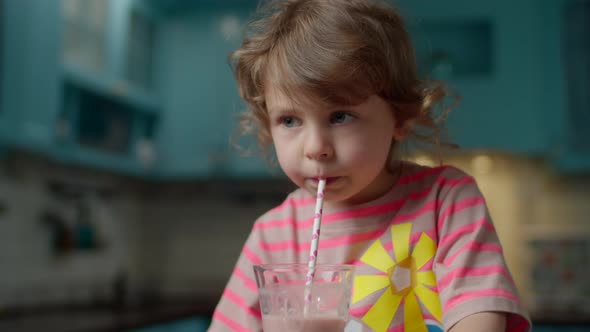 lose up of cute little girl in pink t-shirt drinking berry smoothie with paper straw at home