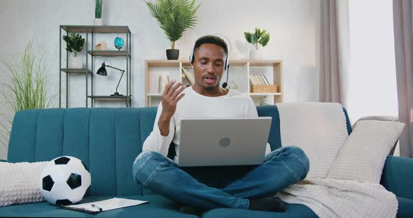Man in Headset which Sitting on the Couch at Home and Holding Video Meeting on Laptop