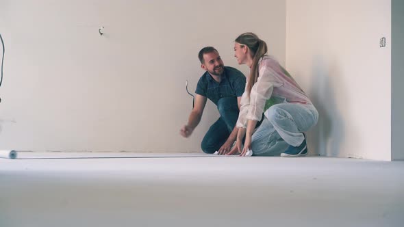 Lovely Couple Unrolls Wallpaper Hugging on Floor in Room