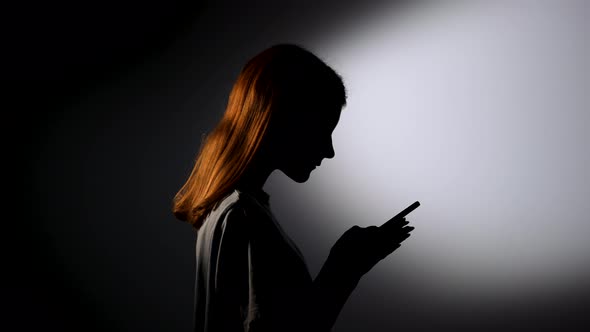 Side View Silhouette of a Young Girl Texting on Her Phone and Being Very Happy