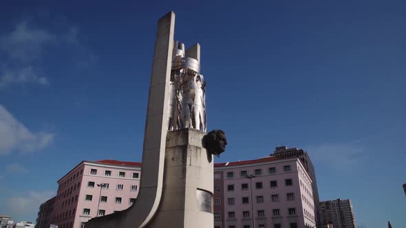 CIRCLING  a statue in a roundabout with buildings in the background and a traffic light on foregroun