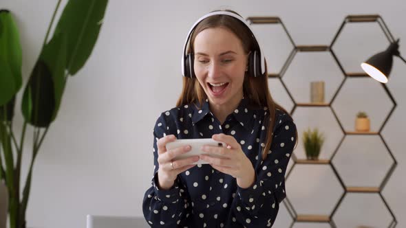 A Young Woman is Playing a Mobile Game with Wireless Headphones While Sitting on the Couch