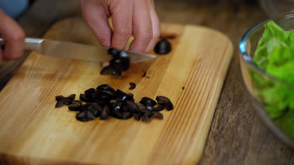 a man cuts black olives. cooking process by the chef. salad ingredients. caring man preparing dinner