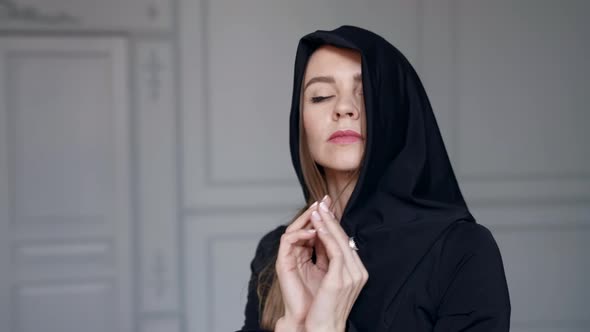 Sexy Lady with Black Hood on Head Posing Dramatically and Looking at Camera in Apartment