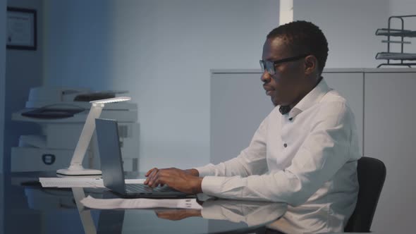 Dolly Push Shot of African Businessman Working on Laptop at Workplace