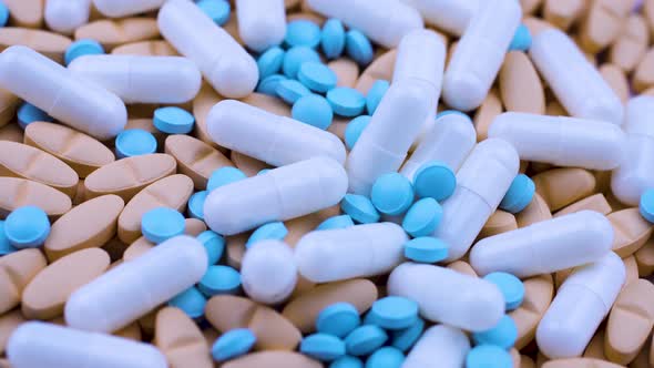 White Capsules Lie on Bright Orange Tablets with Small Blue Painkillers. Rotate