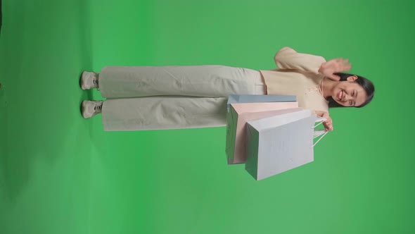 Full View Of Woman Holding Shopping Bags Up Before Waving Hands And Smiling In Front Of Green Screen