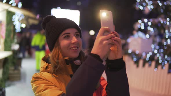 Young Woman in Bright Winter Clothes Taking Photo with Mobile Phone at the Christmas Market