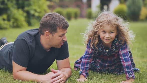 A Cheerful Father and His Daughter Lie on the Grass in the Garden