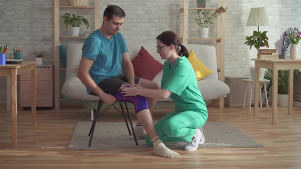 Nurse Helps To Pull the Bandage on the Knee of a Man Athlete