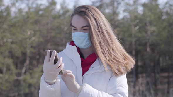 Portrait of Brunette Young Woman in Face Mask and Protective Gloves Talking on the Phone. Brunette