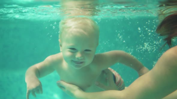 Adorable Toddler is Swimming Under the Water in the Swimming Pool Together with His Mother