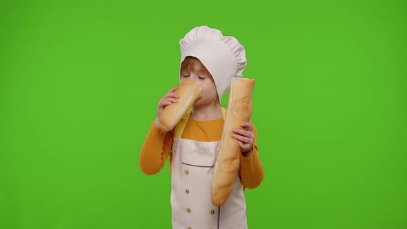 Child Girl Dressed in Apron Like Chef Cook Baker Breaking and Eating Fresh Baguette on Chroma Key