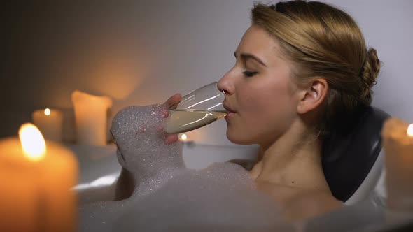 Dreamy Woman Lying in Bath With Foam Bubbles and Candles, Drinking Champagne