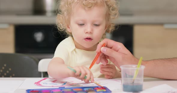 Close Up of a Little Girl Who is Drawing a Red Heart with Watercolors Her Father Helps Her to Fill