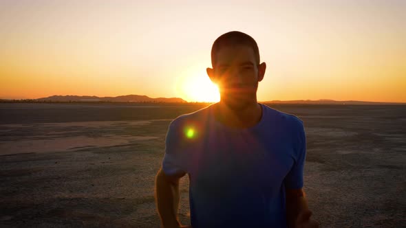 Athletic man working out with battle ropes on a dry lake at sunset