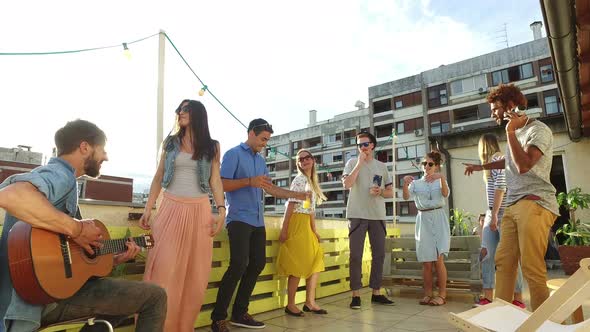 Happy people dancing and playing guitar at the rooftop party on sunny day